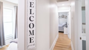 Ein Flur mit einem 'WELCOME'-Schild, Holzboden und einem Bettgestell im Hintergrund.