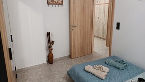Een slaapkamer met een bed, een 'WELCOME' bord, een houten garderobe en een vaas met gedroogde bloemen.