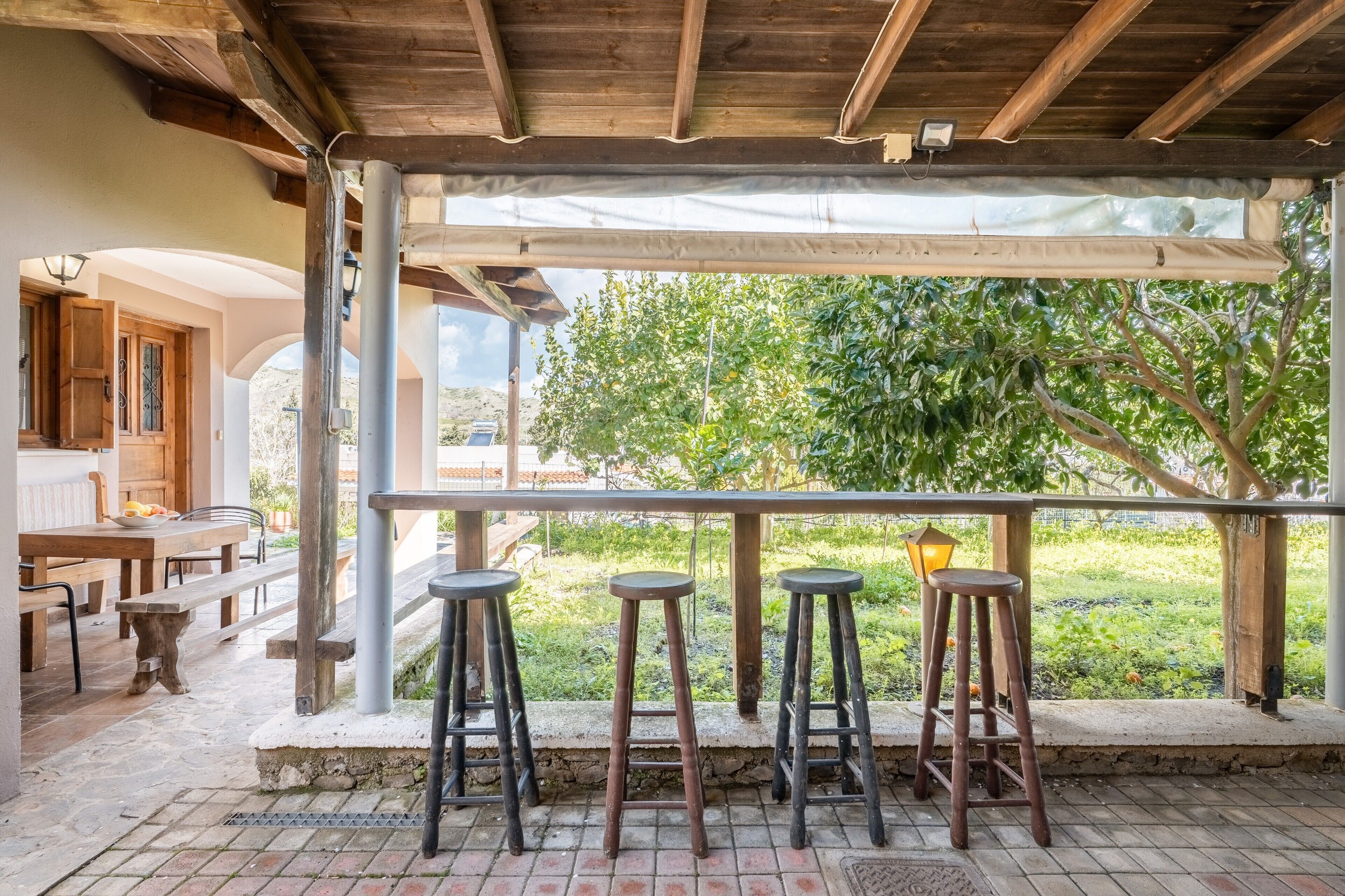 Un patio al aire libre con mobiliario de madera, incluyendo una mesa y bancos, y tres taburetes.