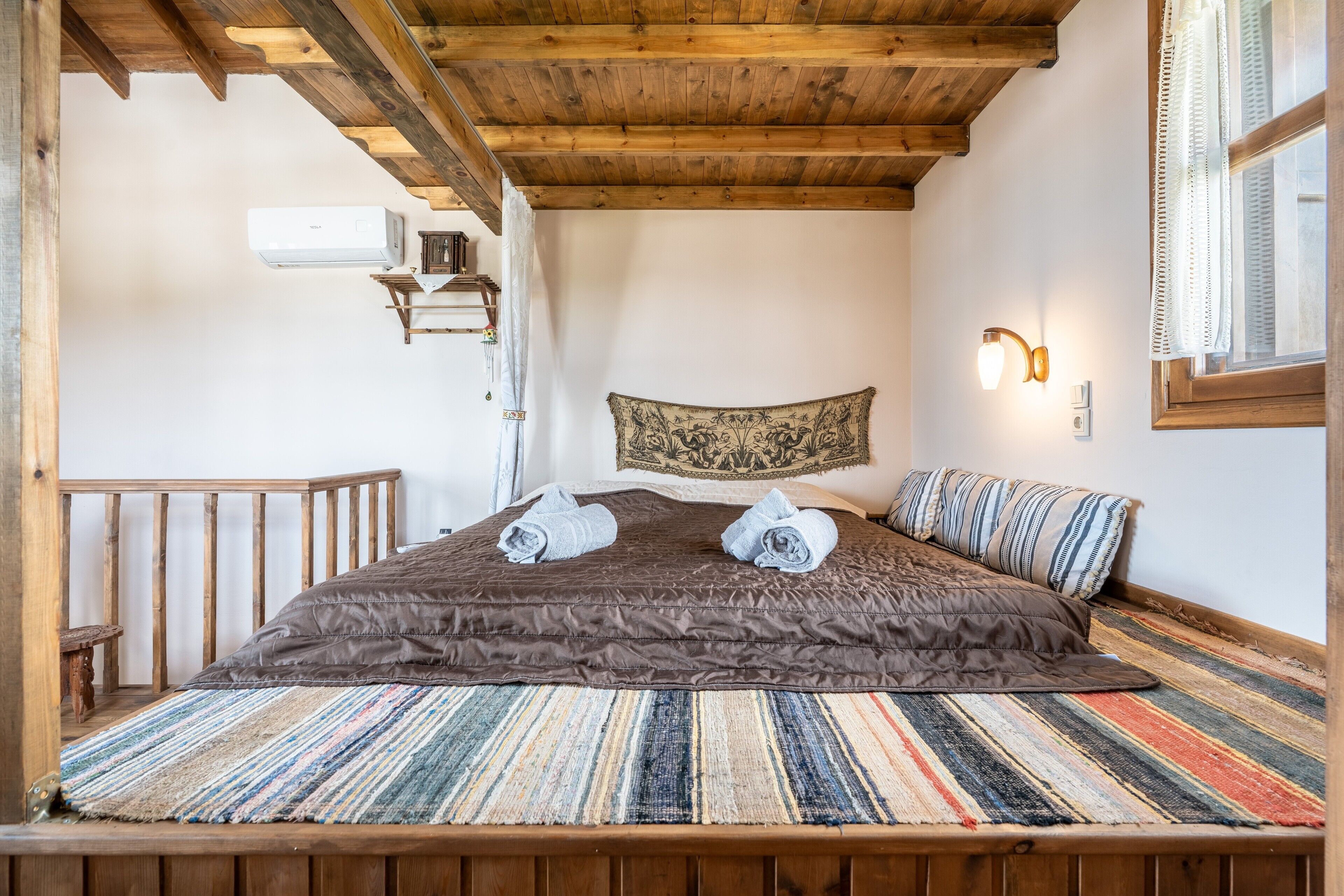 Un dormitorio con techo de madera, una cama con alfombra a rayas, un tapiz y una mesita de noche.