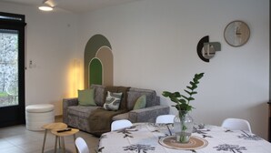 A dining area with a table set for two, a grey sofa with cushions, a white chair, and a small round table. - Recoin Bohème - Pretty, comfortable accommodation - 5 minutes' walk from the Bassin Bleu! (Saint-Benoît)