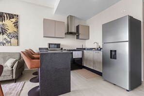 A modern kitchen with a large refrigerator, a microwave, and a gas stove. There is a sofa and a coffee table in the living area. - NOK Cozy 1BR Apartment in Panorama Lake-Punta Cana (Punta Cana)