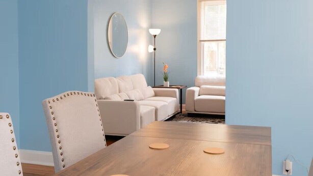 Een woonkamer met een houten eettafel, twee witte banken, een ronde spiegel en een vloerlamp.