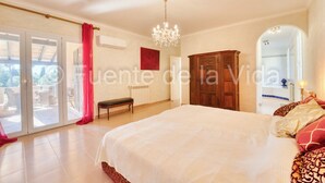 Ein Schlafzimmer mit einem großen Bett, einer Kristallleuchtre, einem Holzschrank und einer Glastür zum Außenbereich.