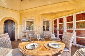 Een eetgedeelte met een ronde tafel voor vier personen, omringd door rieten stoelen, met uitzicht op een binnenterrein door een open boog.