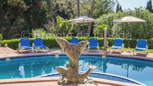 Ein Swimmingpool mit einer zentralen Skulptur, umgeben von Liegestühlen und Sonnenschirmen.