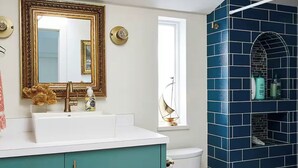 Ein Badezimmer mit einem weißen Waschbecken, türkis-blauen Schränken, einem goldfarbenen Spiegelrahmen, einer weißen Toilette und einem Duschbereich mit blauen Fliesen.