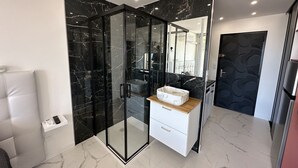 Un bagno moderno con doccia vetrata, pavimento in marmo e un mobile lavabo bianco con lavabo in marmo.