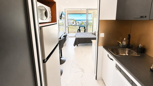 Una cucina compatta con forno a microonde, lavandino e vista su un balcone.