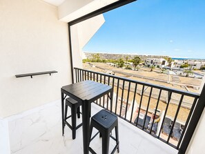 A balcony with a table and two stools, overlooking a beach and a parking area. - Naturiste Cap d'Agde Héliopolis F 68 (Agde)