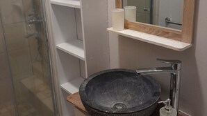 Een badkamer met een glazen douchecabine, een ronde zwarte wastafel, een houten wastafelmeubel en een spiegel met houten lijst.