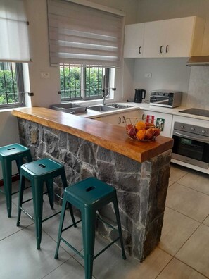 A modern kitchen with a stone island, bar stools, a toaster, and a sink. - Sunny & Cosy Albion (Albion)