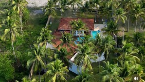 An aerial view of a beachfront property with a small house surrounded by palm trees, a swimming pool, and a sandy beach. - Costa del Sol Beach, El Salvador / Residencia del sol (La Paz)