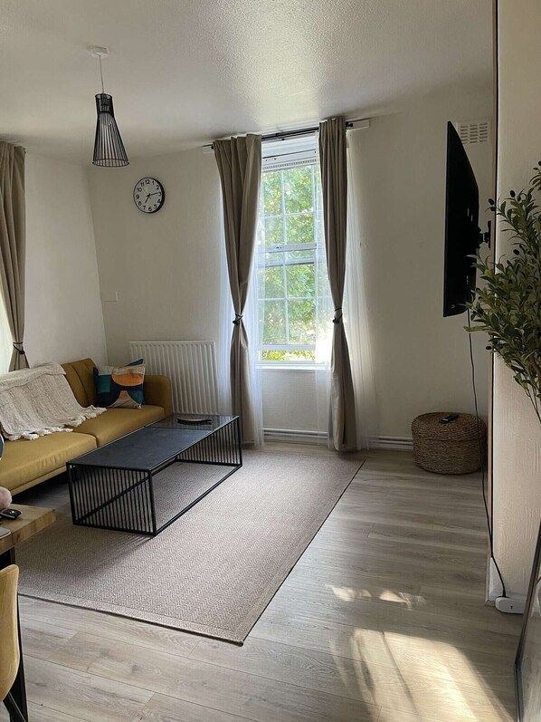 A modern living room with a sofa, coffee table, and a large window with curtains. - London Bliss Retreat (London)