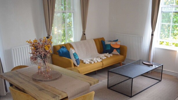 A living room with a yellow sofa, a wooden coffee table, and a vase with flowers. - London Bliss Retreat (London)