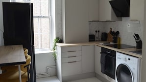 A compact kitchen with a built-in washing machine, a dining area with a table and chairs, and a window with a view of the city. - London Bliss Retreat (London)