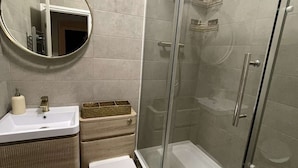A modern bathroom with a glass-enclosed shower, a round mirror, a white sink, and a toilet. - London Bliss Retreat (London)