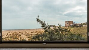 A view through a window of a beach with a building in the distance. - Apartment 'Bellavista Sul Mare' with Sea View, Wi-Fi and Air Conditioning (Palermo)