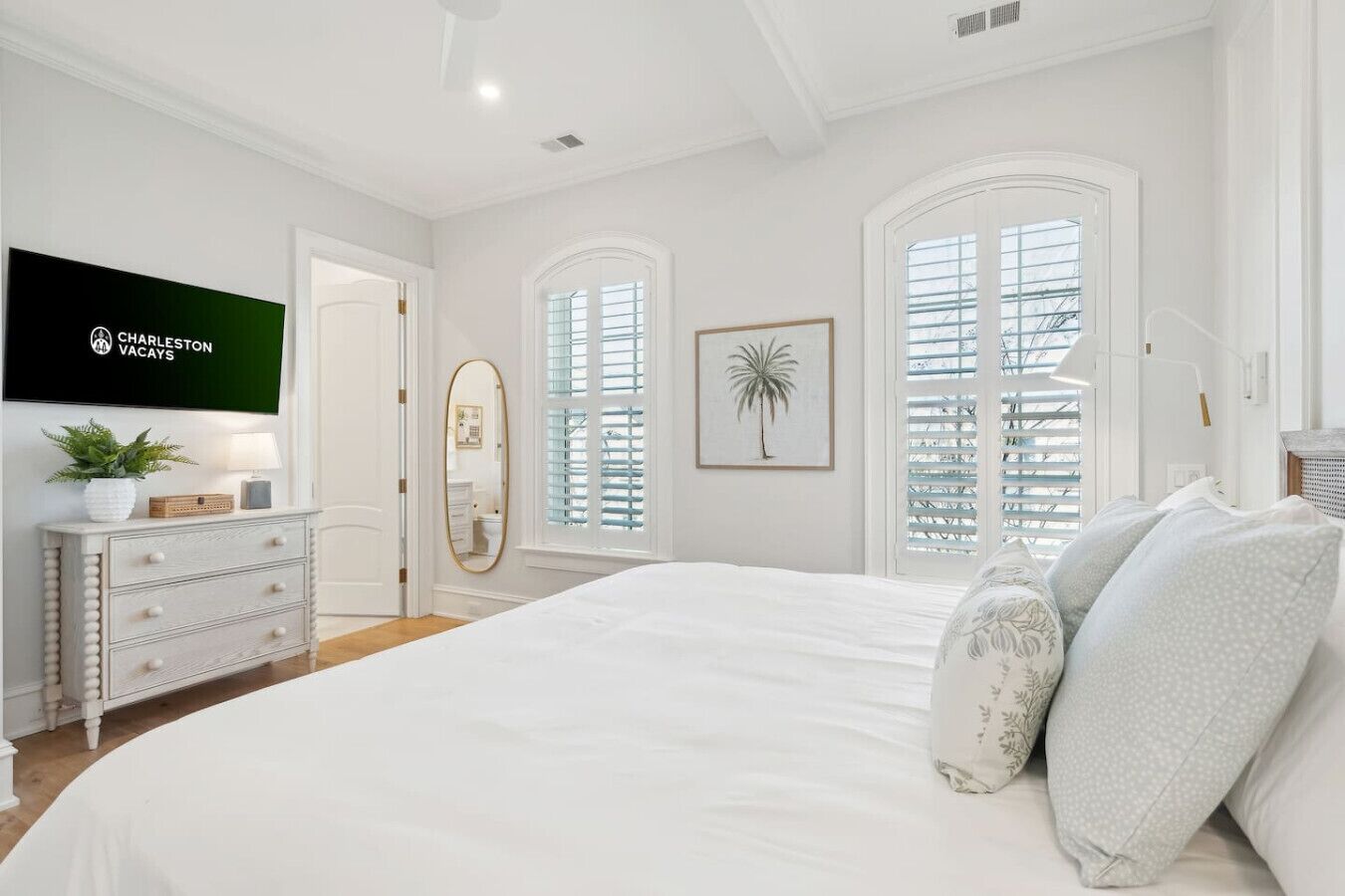 A bedroom with a large bed, a dresser, a TV, and two windows with shutters.