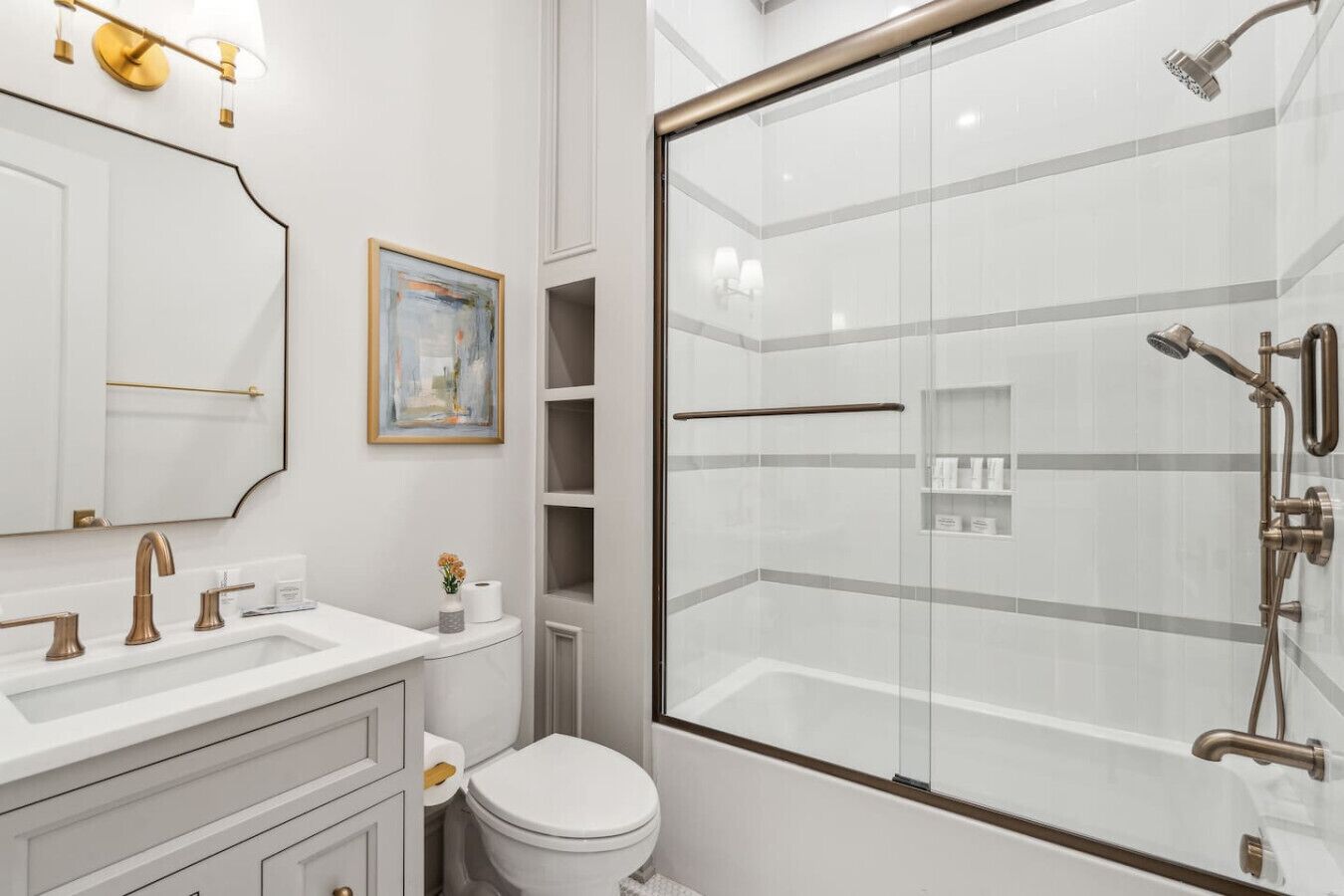 Ein modernes Badezimmer mit einer gläsernen Duschkabine, einem weißen Waschbecken mit goldfarbenen Armaturen und einer Toilette.