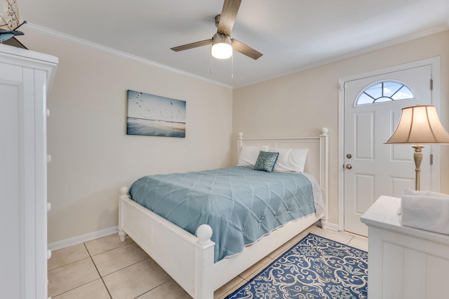 A bedroom with a bed, a ceiling fan, a door, and a lamp.