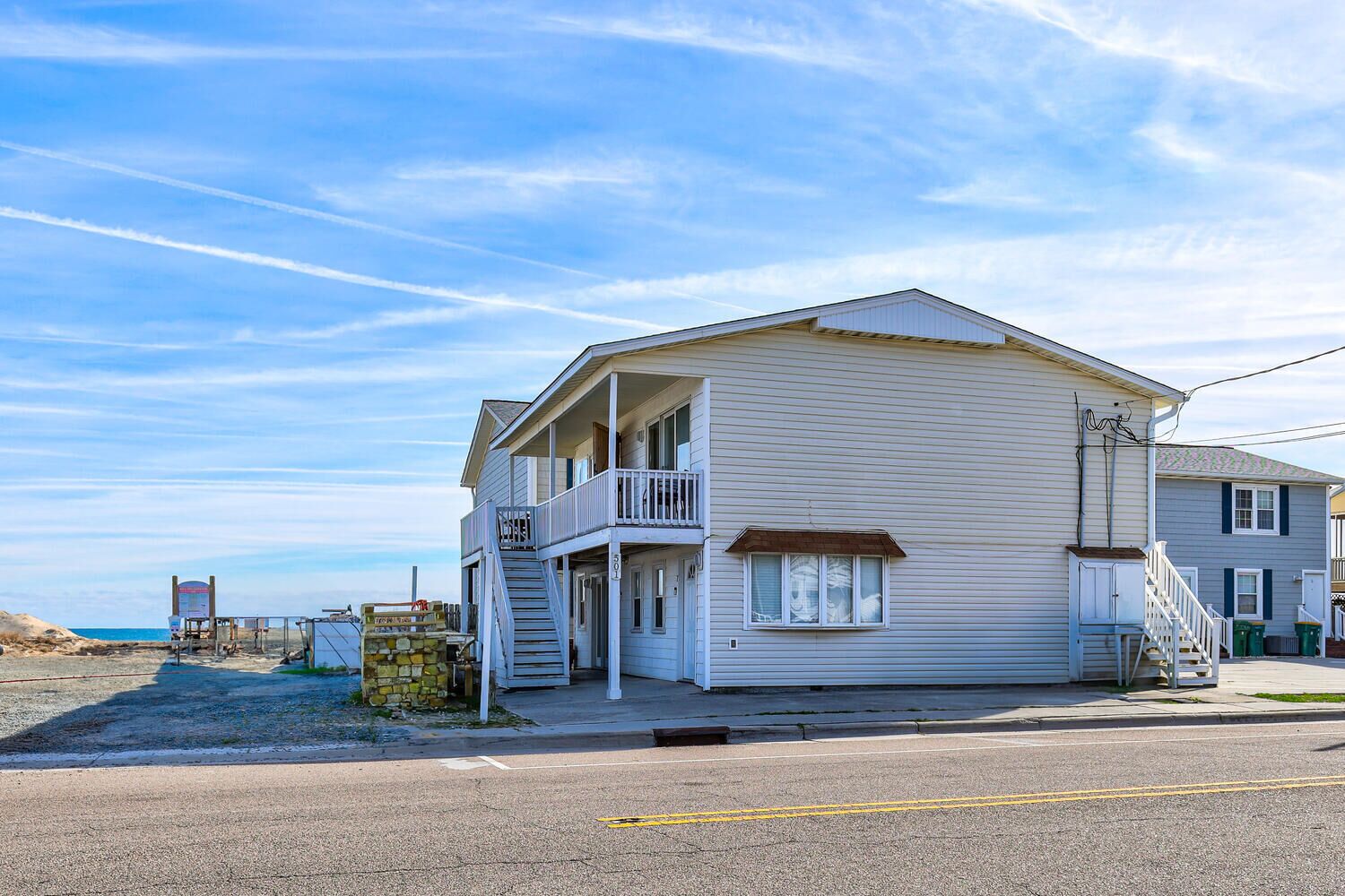 A two-story beach house with a balcony, a staircase leading to the second floor, and a view of the beach.