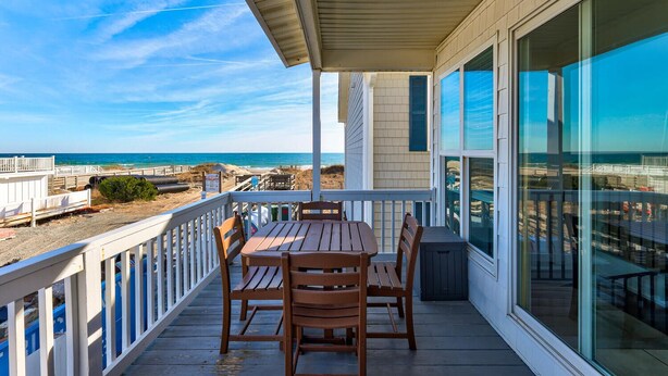 A wooden deck with a table and chairs overlooking a beach. - Seaview 6&7: 3 Bedroom Duplex in Kure Beach (Kure Beach)