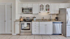 A modern kitchen with white cabinetry, a stainless steel stove, a microwave, a dishwasher, and a refrigerator. - Seaview 6&7: 3 Bedroom Duplex in Kure Beach (Kure Beach)
