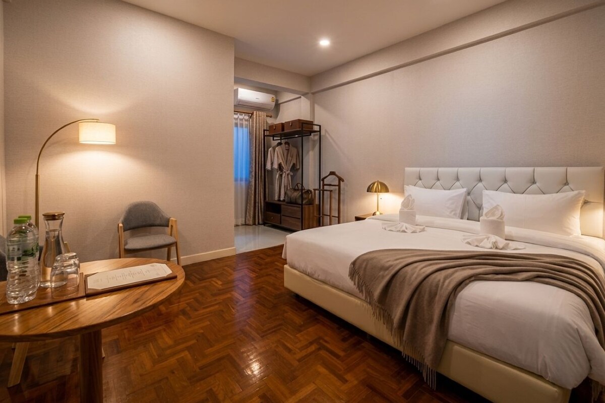Ein Hotelzimmer mit einem großen Bett, Nachttischlampen, Holzboden und einem kleinen Tisch mit Lampe und Wasserflaschen.