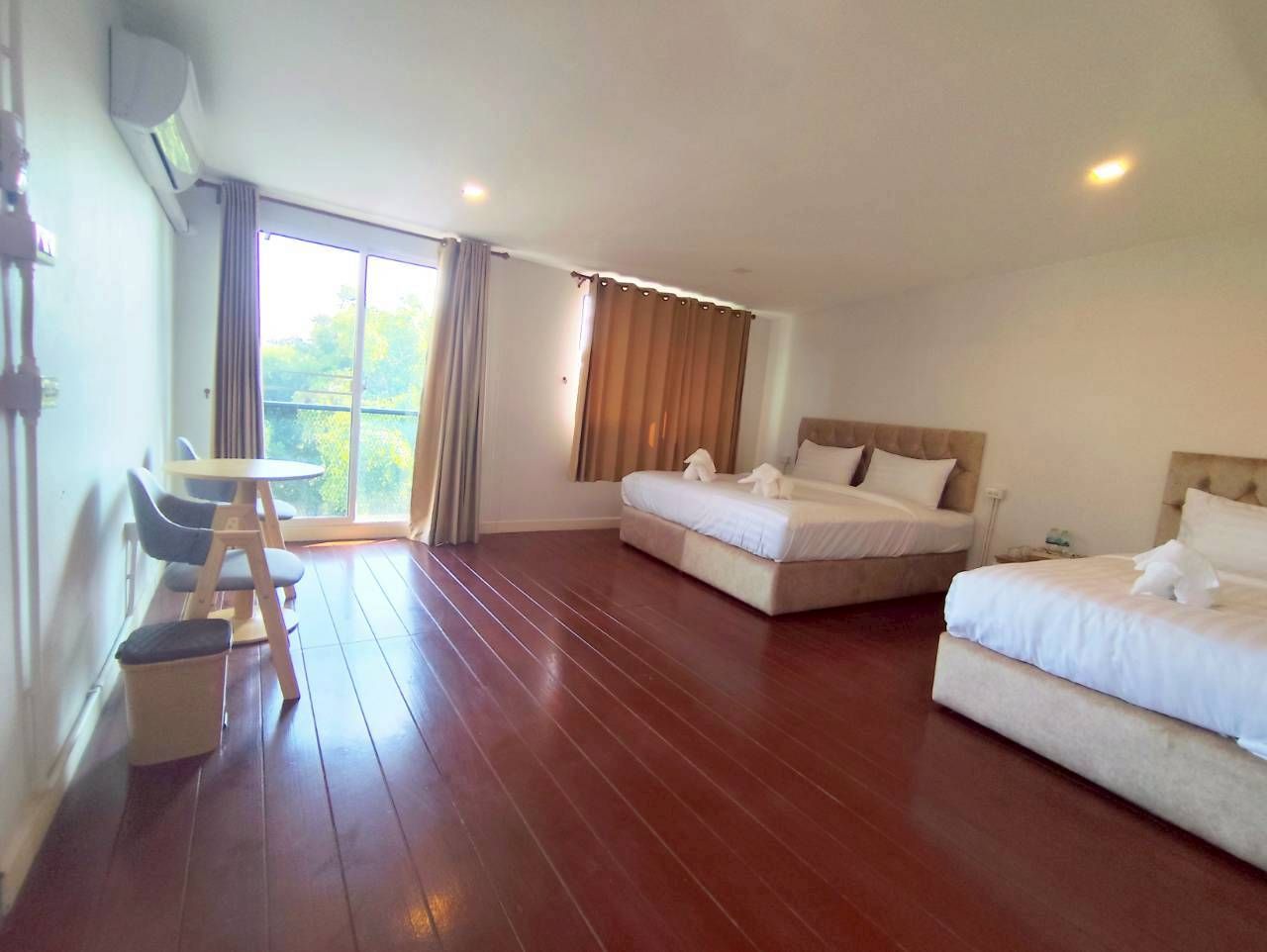 A hotel room with a large bed, a smaller bed, a desk with chairs, and a view of the outdoors through a window.