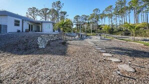 A modern building with a covered outdoor area, surrounded by trees and a gravel path. - Cozy Tiny Home Studio - Myakka Forest (Port Charlotte)