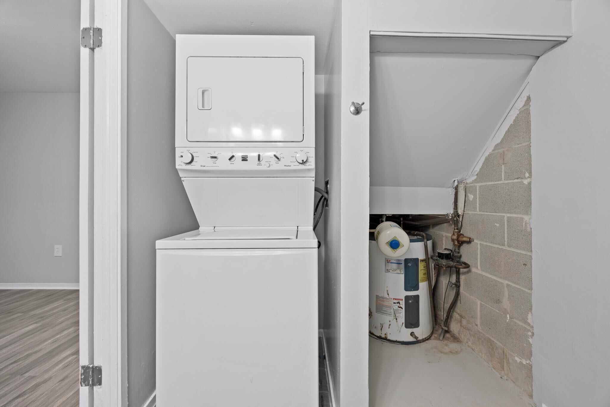 A compact laundry room with a stacked washer and dryer, a water heater, and a visible plumbing system.