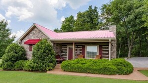 A log cabin with a stone exterior, a red awning, and a porch with two chairs. - Uncle Pete`s Cabin ~ Rockhaven (Mount Juliet)