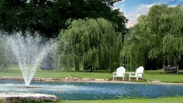 Eine friedliche Außenanlage mit einem Brunnen, zwei weißen Stühlen und üppiger Bepflanzung.