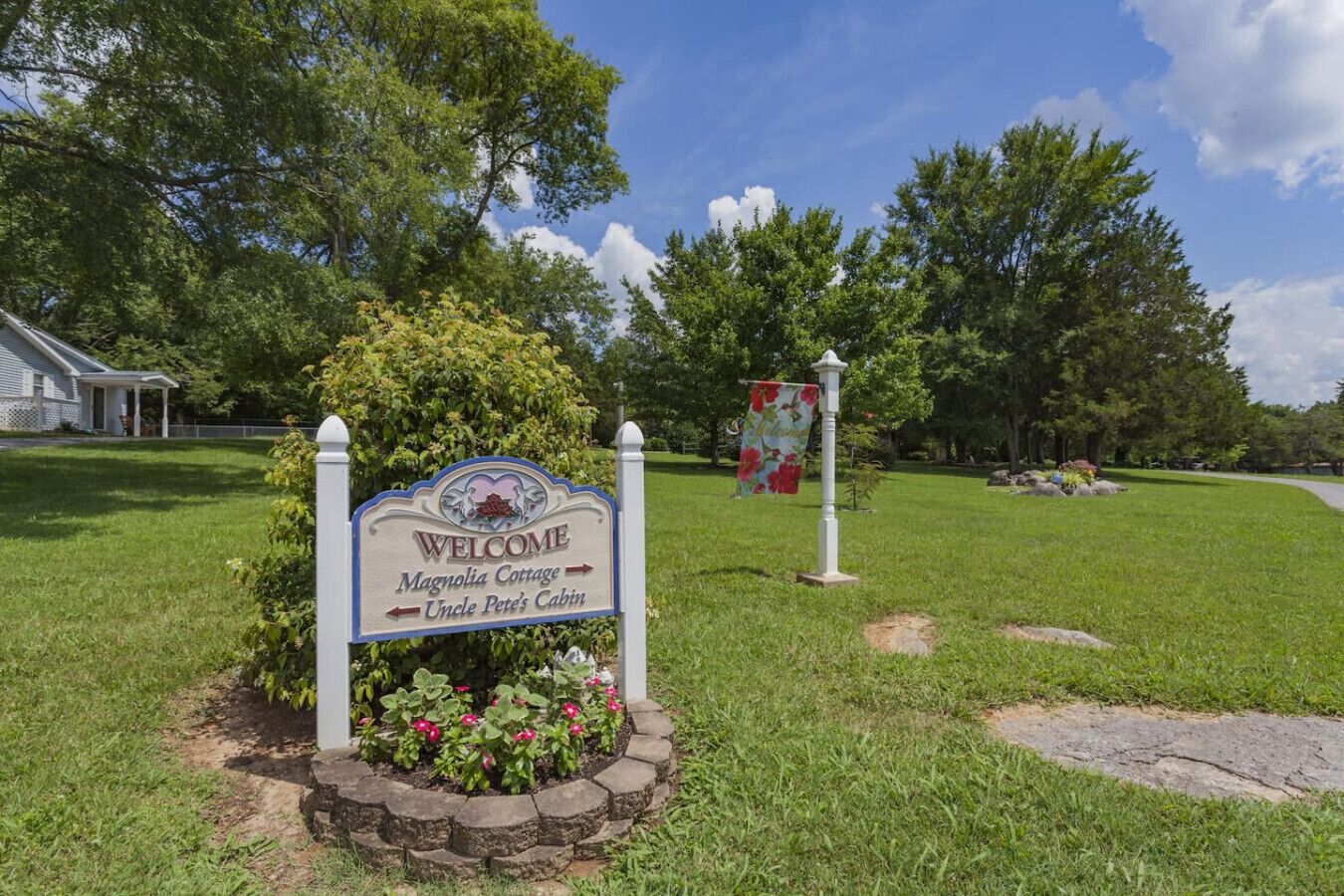 A welcome sign for Magnolia Cottage and Uncle Pete's Cabin, surrounded by a well-maintained lawn and trees.