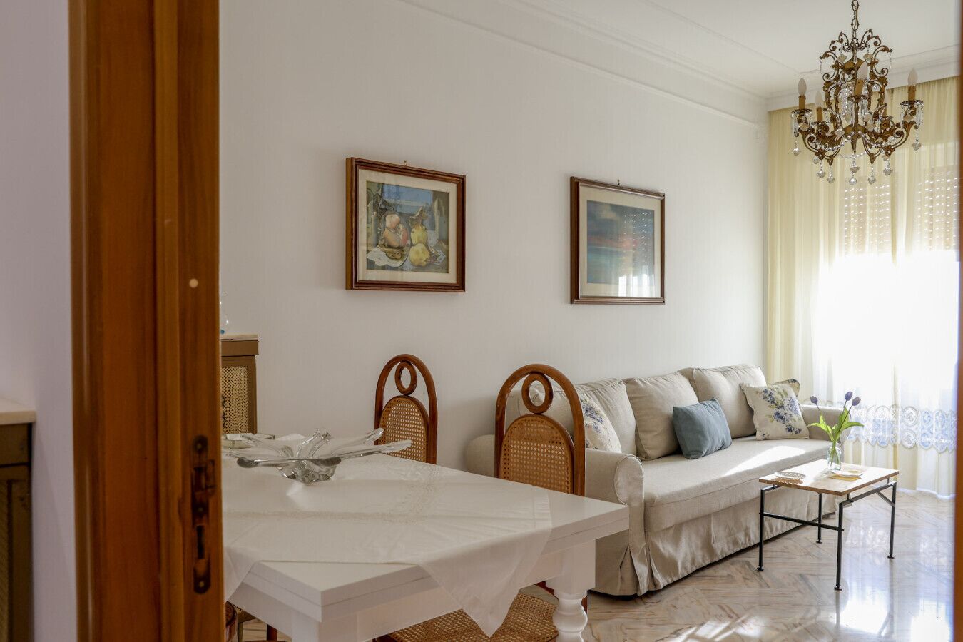 A living room with a sofa, a dining table, and two framed artworks on the wall.