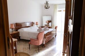 A spacious bedroom with a large bed, a wooden wardrobe, a bedside table with a lamp, a mirror, and a wicker chair. - Alla Brezza Blu - Mola di Bari (Mola di Bari)