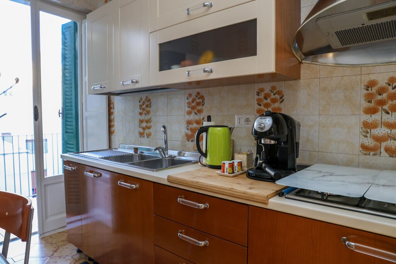 A kitchen with a sink, a green kettle, and a coffee maker on the counter.