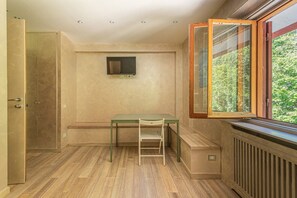 Ein Zimmer mit Holzboden, einem Tisch mit Stuhl, einem Heizkörper und einem Fenster mit Blick auf Grünflächen.