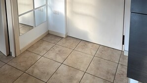 Una habitación con una puerta blanca, un portero automático en la pared y suelo de baldosas.