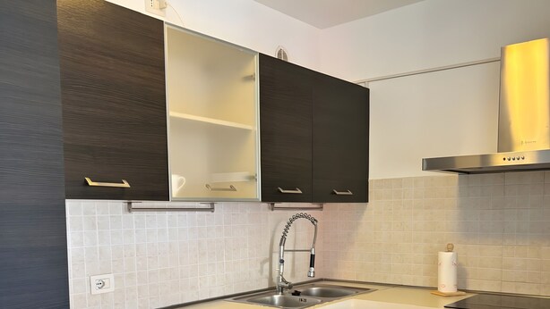 Una cocina moderna con gabinetes oscuros, un lavamanos de acero inoxidable y un horno empotrado.