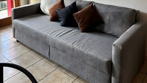 Un sofá gris con tres cojines, un radiador y dos cuadros enmarcados en la pared.