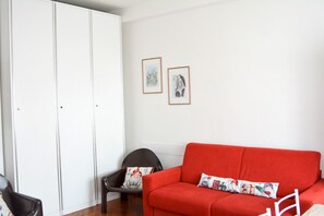 Ein Zimmer mit einem roten Sofa, einem weißen Kleiderschrank und zwei gerahmten Bildern an der Wand.