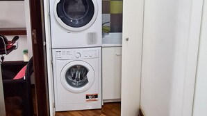 Kompakti pyykinhuone, jossa on kaksi pesukonetta, pieni työtaso ja tuoli.