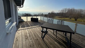 A wooden deck with a table and chairs, overlooking a lake and mountains. - 5-star maisonette vacation apartment Maria with fantastic Black Forest views (Schramberg)