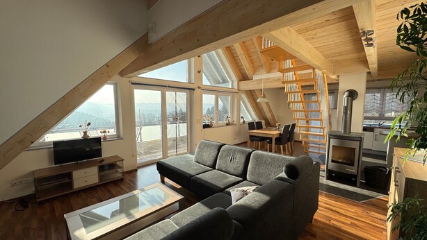 A spacious loft with a large living area, a dining table, and a kitchen with a wood-burning stove. - 5-star maisonette vacation apartment Maria with fantastic Black Forest views (Schramberg)