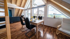 A dining area with a wooden table and chairs, large windows, and a view of the outdoors. - 5-star maisonette vacation apartment Maria with fantastic Black Forest views (Schramberg)