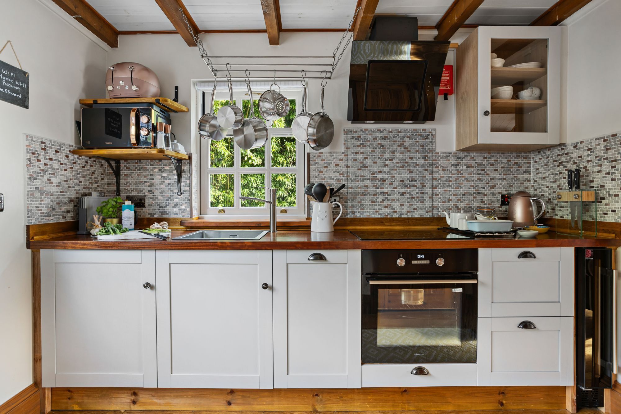 A kitchen with white cabinets, a wooden countertop, a hanging pot rack, and a brick backsplash.