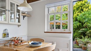 Un comedor con una mesa de madera, sillas y un ventanal con vista a follaje.