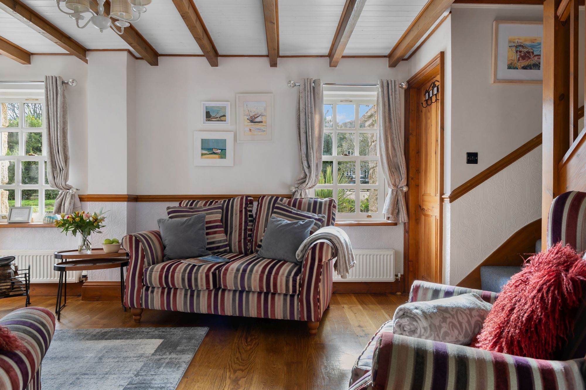 Ein gemütliches Wohnzimmer mit einem gestreiften Sofa, Holzboden und einer Treppe, die in eine andere Ebene führt.